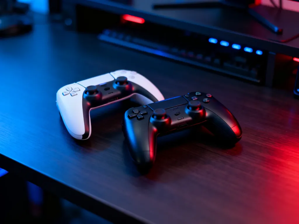Biała konsola Asus ROG Ally oraz czarny Steam Deck leżące obok siebie na biurku w klimatycznym, gamingowym oświetleniu.
